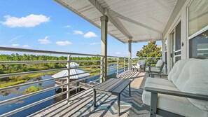 Une terrasse extérieure couverte avec vue sur une rivière et une forêt, comprenant un belvédère, un espace salon et une rambarde.