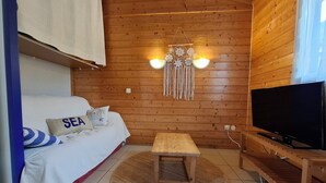 A cozy room with a bed, a small wooden table, a TV, and a wall hanging. - Caban'Océan, the ideal way to discover the Landes Coast between Sea Spray and Pines (Vielle-Saint-Girons)