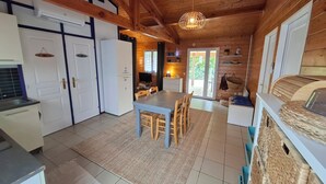 A compact kitchen with white cabinets, a dining area with a table and chairs, and a wooden ceiling. - Caban'Océan, the ideal way to discover the Landes Coast between Sea Spray and Pines (Vielle-Saint-Girons)