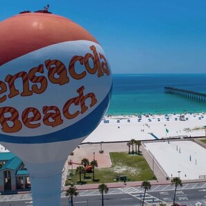 A beachside view with a large water bottle labeled 'Pensacola Beach' and a pier in the background.