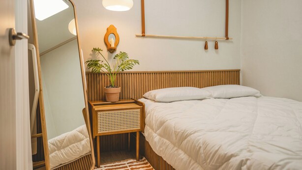 A bedroom with a bed, a bedside table with a potted plant, a mirror, and a hanging light fixture.