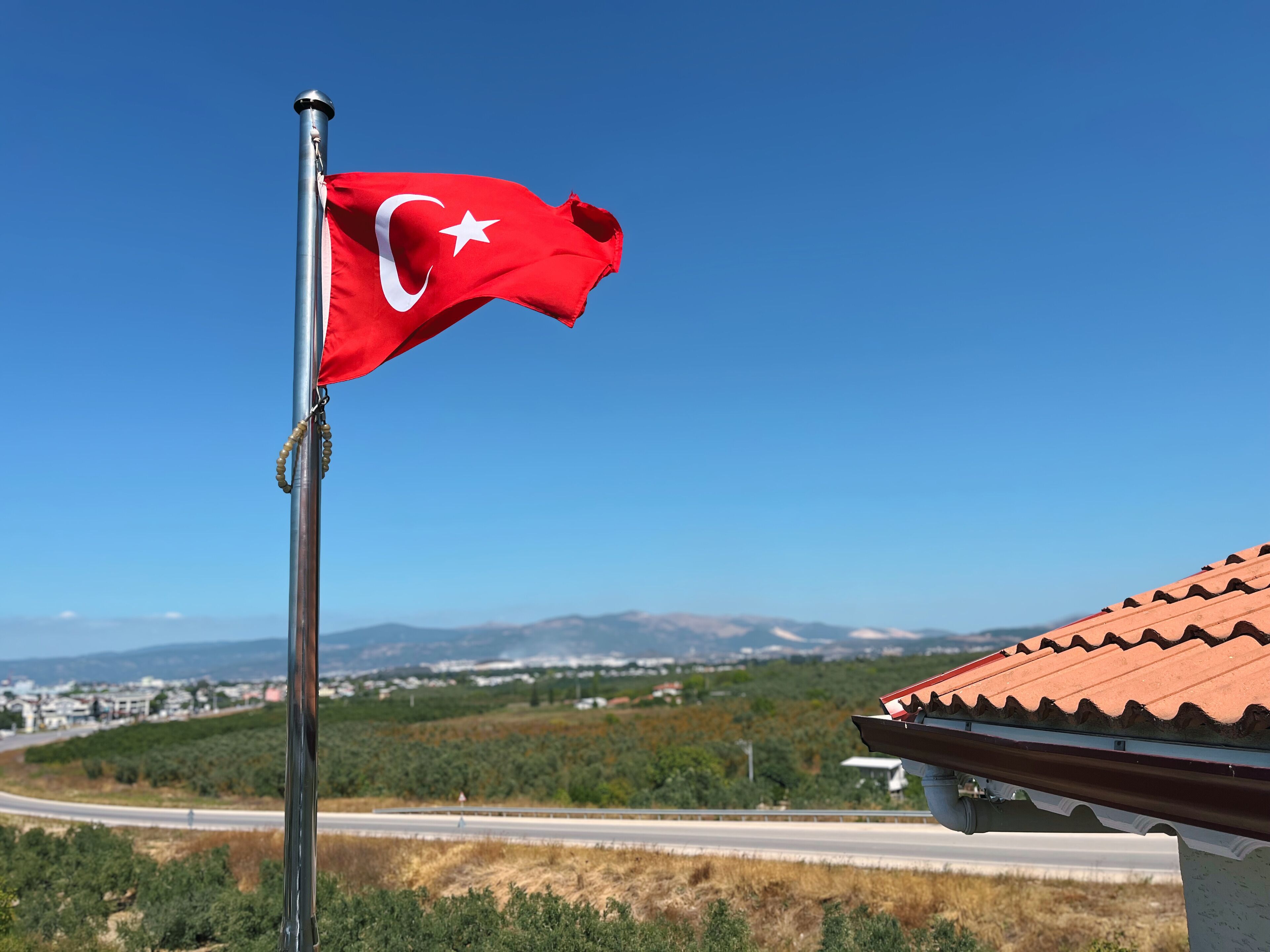 A flagpole with a red flag featuring a white star and crescent, set against a clear blue sky.