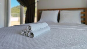 Un lit bien fait, avec du linge de lit blanc et des oreillers, une tête de lit en bois et une fenêtre avec des rideaux.
