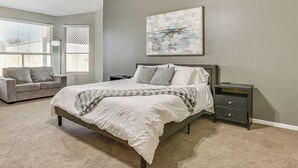 Un dormitorio con cama, mesita de noche, cómoda, ventana con persianas y un cuadro en la pared.