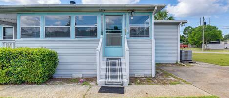 A small, single-story building with a front door, a small porch, and a visible air conditioning unit.