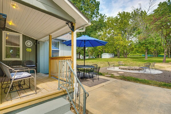 A covered patio with outdoor furniture, a blue umbrella, and a fire pit.