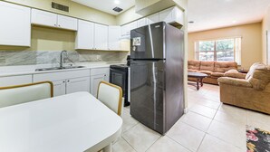 A compact kitchen with white cabinets, a stainless steel refrigerator, and a dining area with a white table and chairs.