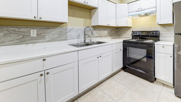 A kitchen with white cabinets, a stainless steel sink, a black oven, and a refrigerator.