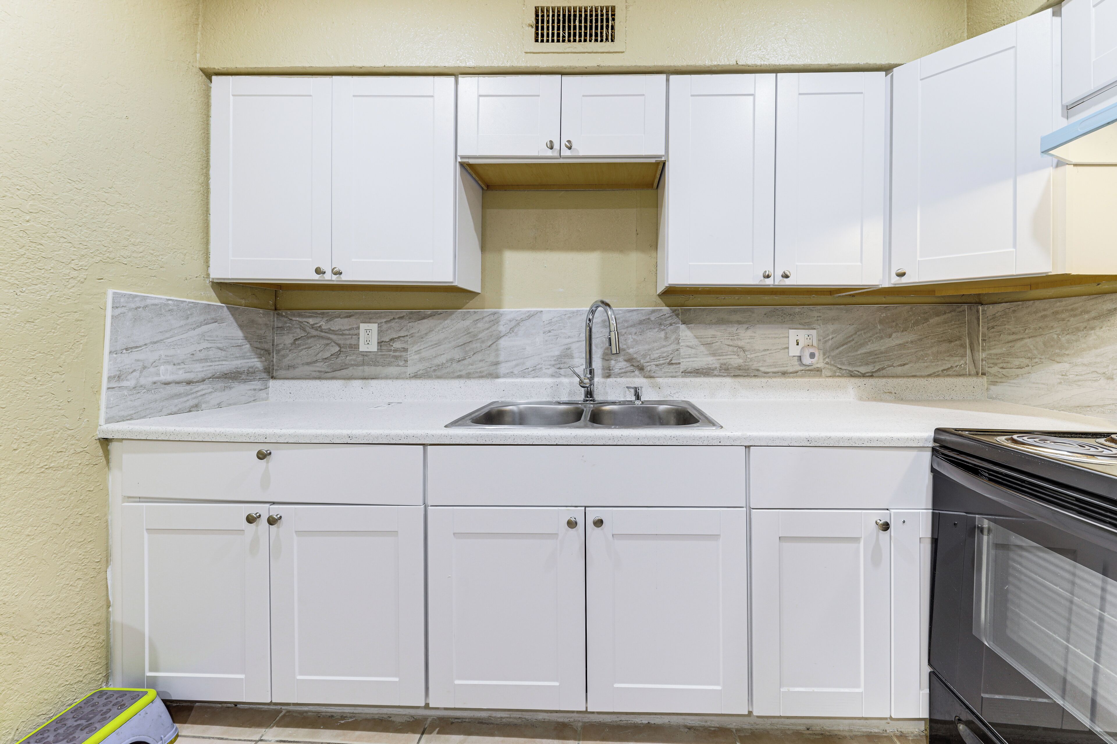A kitchen with white cabinets, a stainless steel sink, and a black oven.