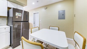 A compact kitchen with a stainless steel refrigerator, a white dining table, and four chairs with wooden armrests.