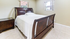 A bedroom with a bed, a nightstand, and two windows.