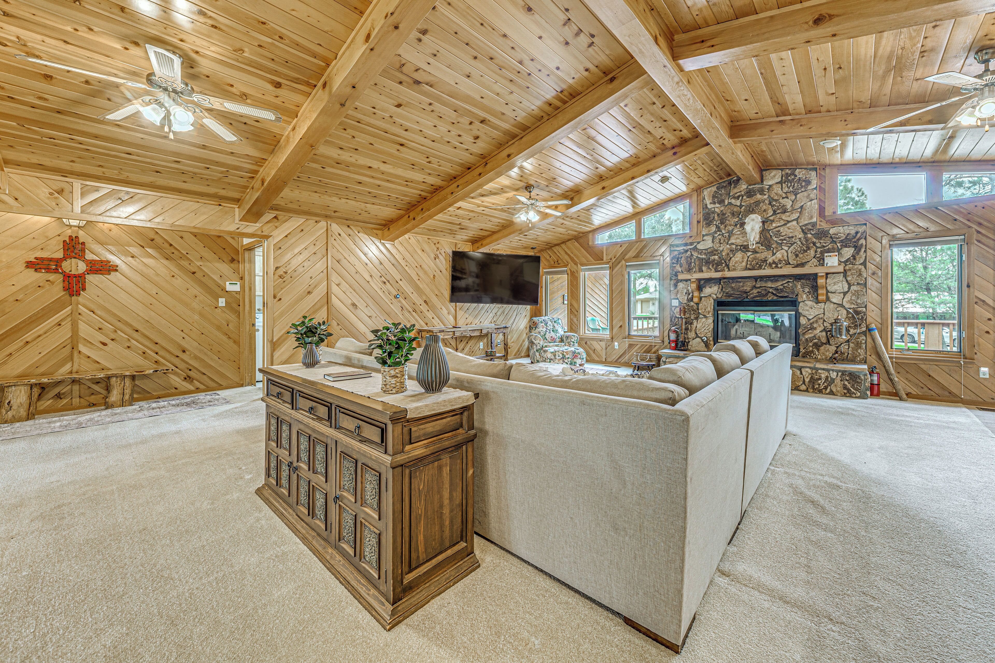 A spacious living room with a stone fireplace, wooden ceiling beams, and a large window.