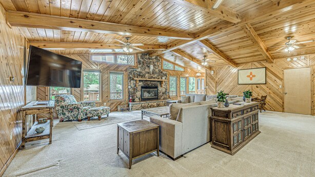 A spacious living room with a stone fireplace, wooden ceiling, and large windows. - Hot Tub & Deck: Home 1 Mi to Ruidoso River! (Ruidoso)