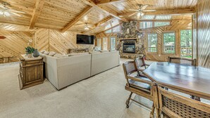 A spacious living room with a large wooden ceiling, a stone fireplace, a flat-screen TV, and a dining area with a wooden table and chairs. - Hot Tub & Deck: Home 1 Mi to Ruidoso River! (Ruidoso)