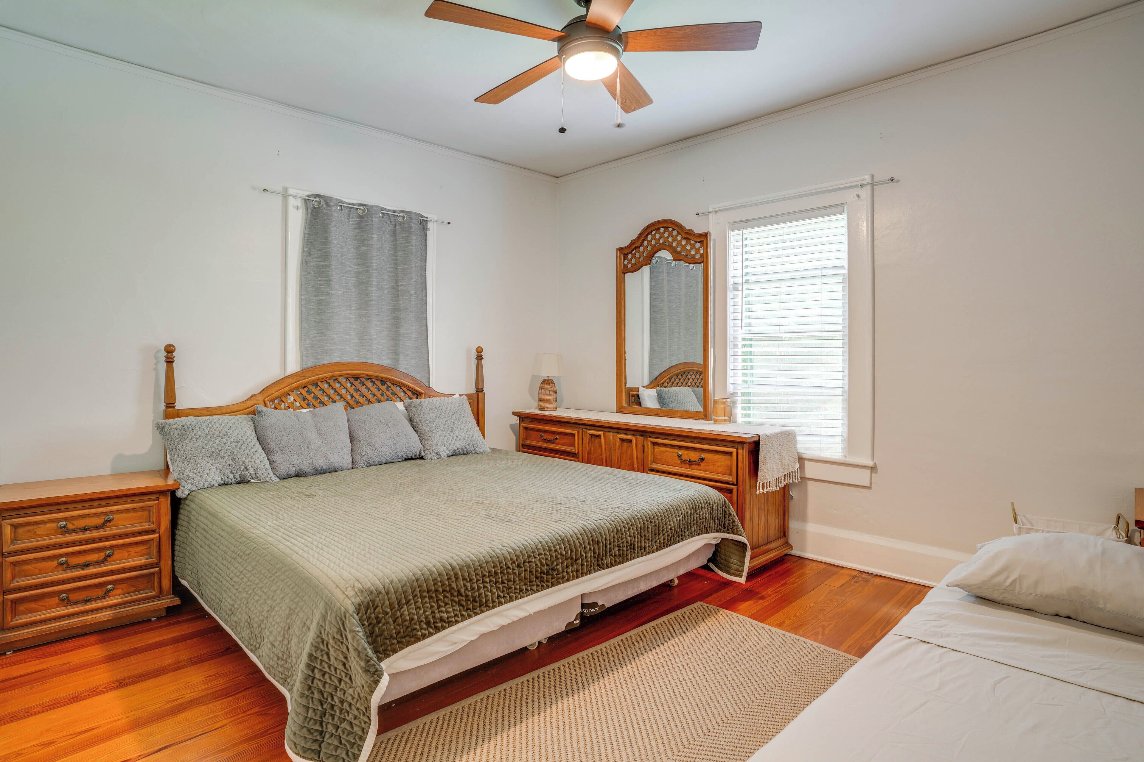 A bedroom with a wooden bed, a nightstand, a dresser, a mirror, and a ceiling fan.