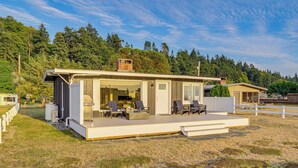 Una casa moderna con una amplia terraza, mobiliario exterior y vistas a una ladera boscosa.