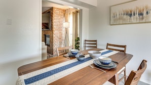 Un coin repas avec une table en bois, des chaises et un chemin de table bleu et blanc à rayures. On y trouve un mur en briques et un tableau accroché au mur.