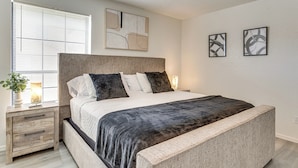 Une chambre à coucher avec un grand lit, des tables de chevet, une commode et une fenêtre avec des stores.