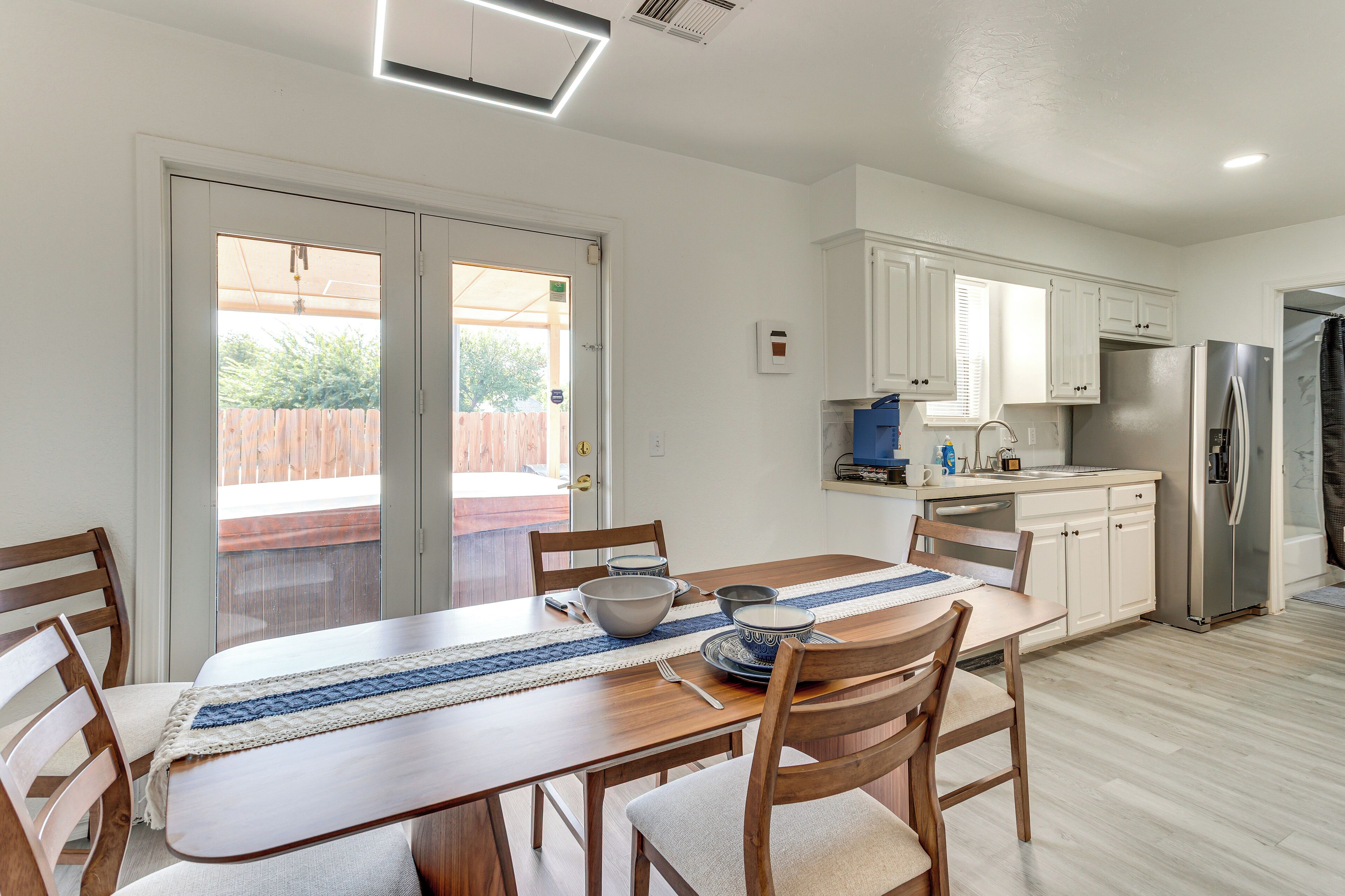 A modern kitchen with white cabinets, a stainless steel refrigerator, and a dining area with wooden chairs and a table.
