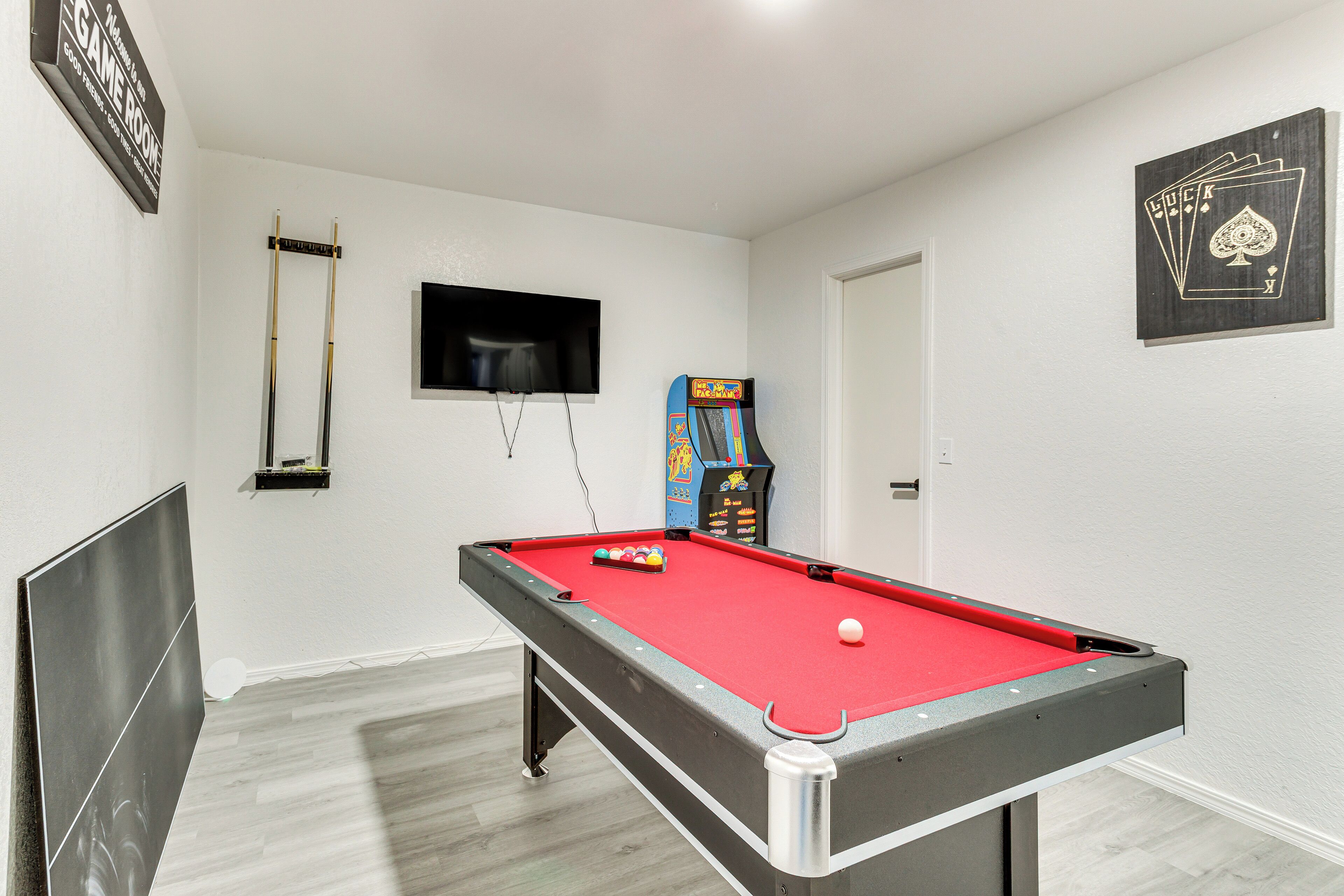 Une table de billard recouverte d’un drap de feutre rouge, un téléviseur fixé au mur et un emplacement pour une machine de jeu à pièces.