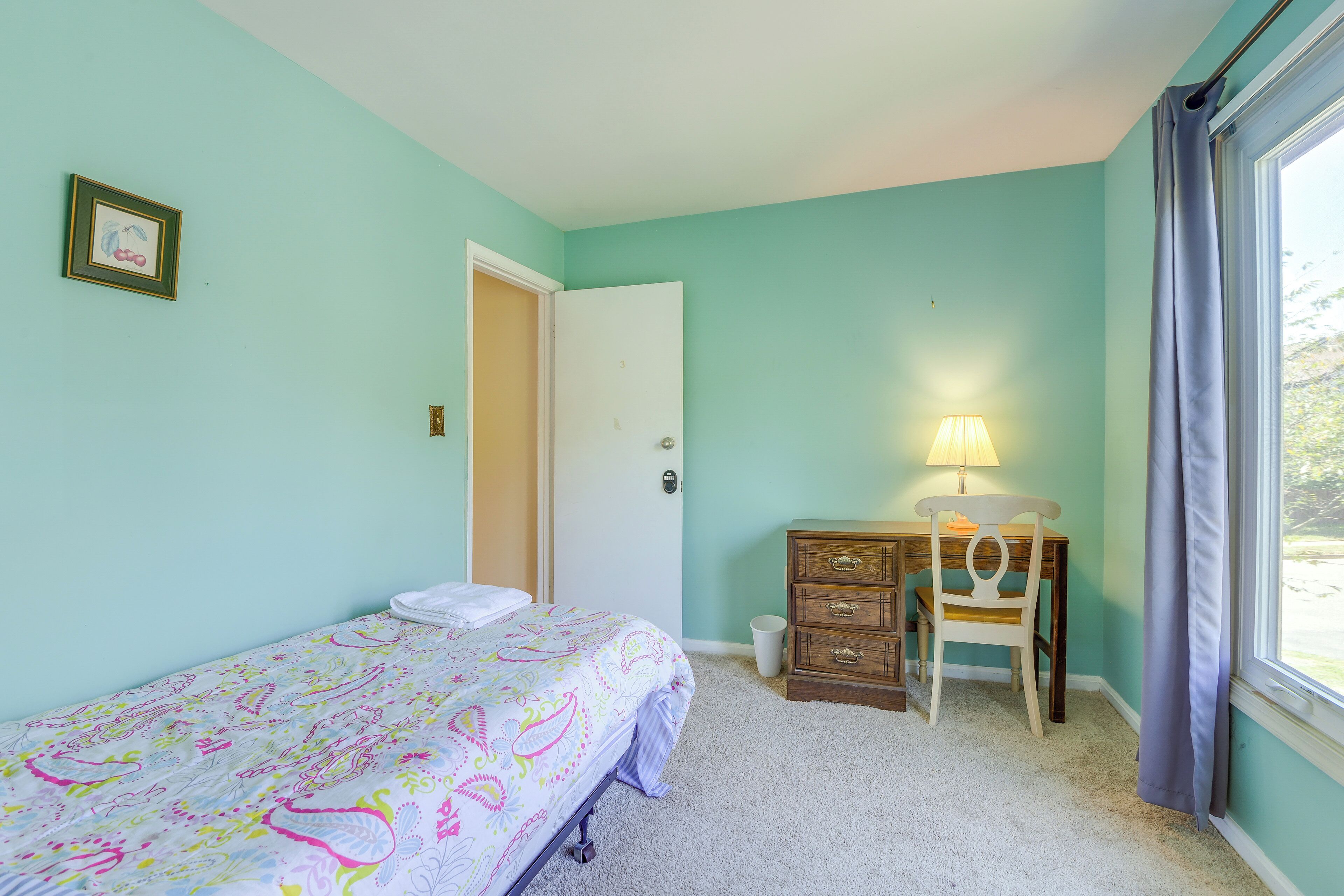 A bedroom with a bed, a desk with a chair, a lamp, and a window with curtains.