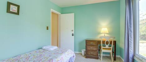 A bedroom with a bed, a desk with a chair, a lamp, and a window with curtains.