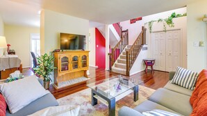 A living room with a sofa, a glass coffee table, a wooden cabinet, a television, and a staircase. - Close to Hospital & Dulles: Herndon Townhome (Herndon)