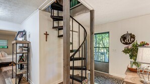 A staircase with a wooden handrail and black metal balusters, a bookshelf, a cross on the wall, and a 'hello' sign with greenery. - Hiwassee River Gem w/ Huge Decks: Great for Groups (Hiawassee)