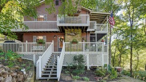 A two-story house with a white picket fence, a front porch, and a staircase leading to the entrance. - Hiwassee River Gem w/ Huge Decks: Great for Groups (Hiawassee)