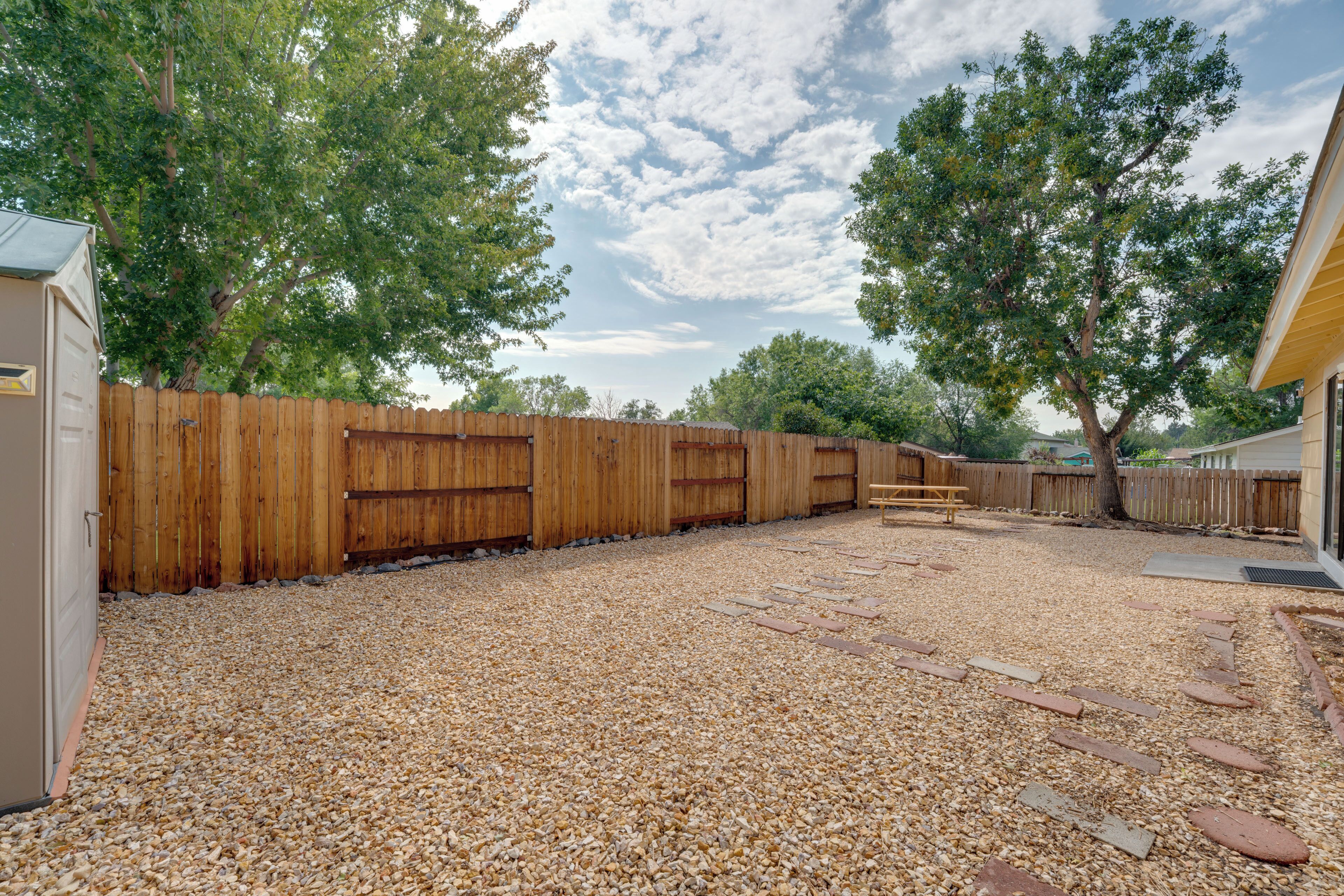 A backyard with a wooden fence, gravel ground, and a bench.