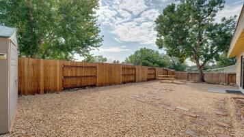 A backyard with a wooden fence, gravel ground, and a bench.