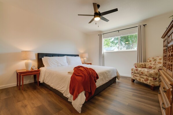 A bedroom with a bed, a nightstand, a chair, a ceiling fan, and a window.