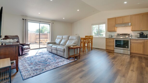 A spacious living area with a sofa, dining table, and chairs, a kitchen with wooden cabinets and appliances, and a large sliding glass door leading to an outdoor patio. - Quiet & Convenient Sparks Retreat Near I-80 & Reno (Sparks)