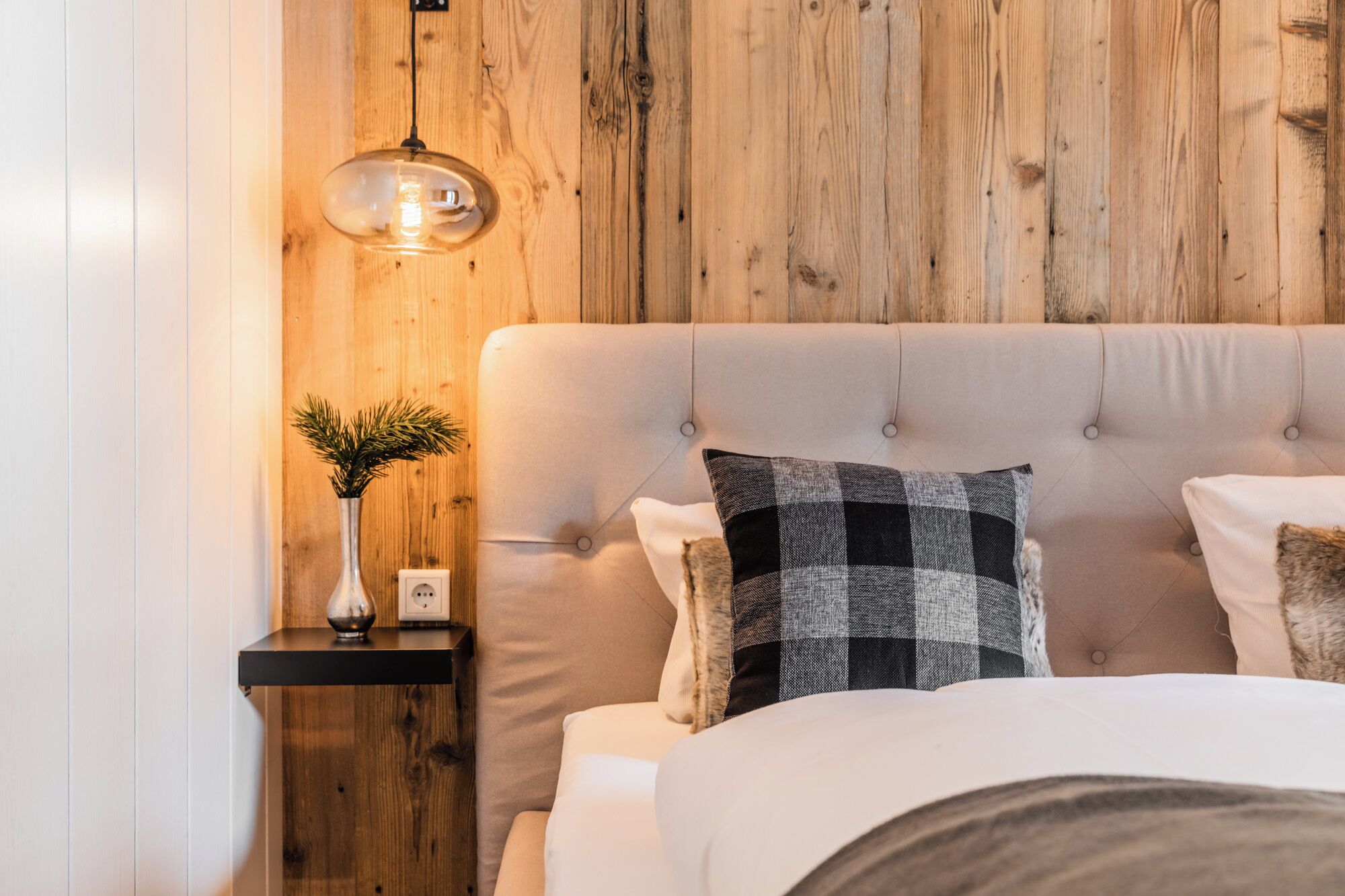 Ein Schlafzimmer mit einer Holzwand, einem Nachttisch mit einer Vase und einer Lampe sowie einem Bett mit vielen Kissen.