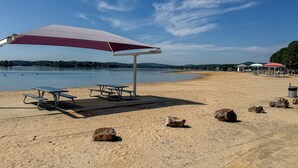 A beach with picnic tables and a large umbrella. - Golf, Fish & Hike: Hot Springs Village Home! (Hot Springs Village)