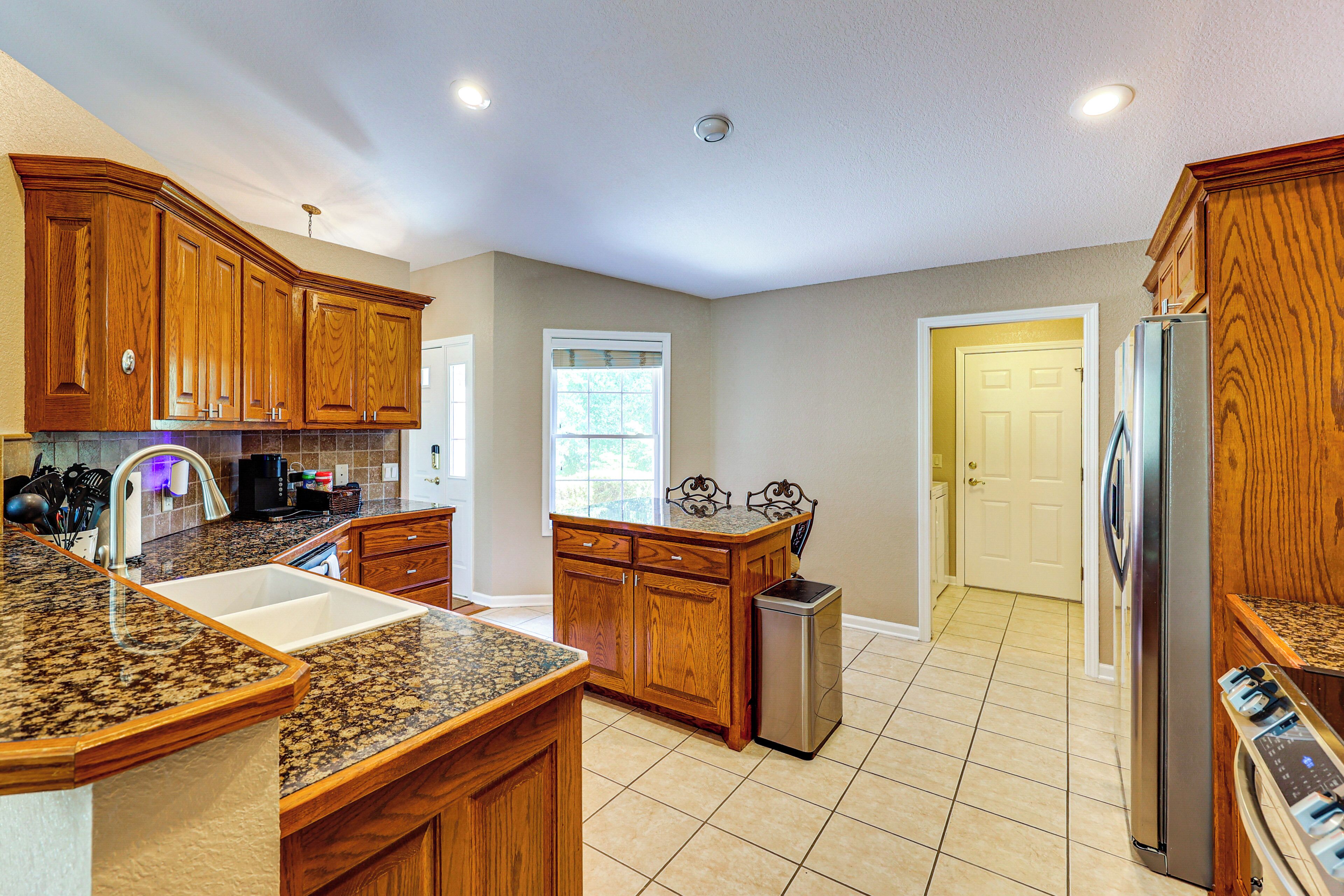A kitchen with wooden cabinets, granite countertops, stainless steel appliances, and a tiled floor.