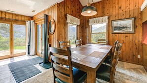 Ein Esszimmer mit Holzwänden, einem großen Tisch, Stühlen, großen Fenstern und einem gerahmten Bild an der Wand.