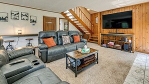 Ein Wohnzimmer mit einer Couch, einem Couchtisch und einem an einer Holzwand montierten Fernseher.