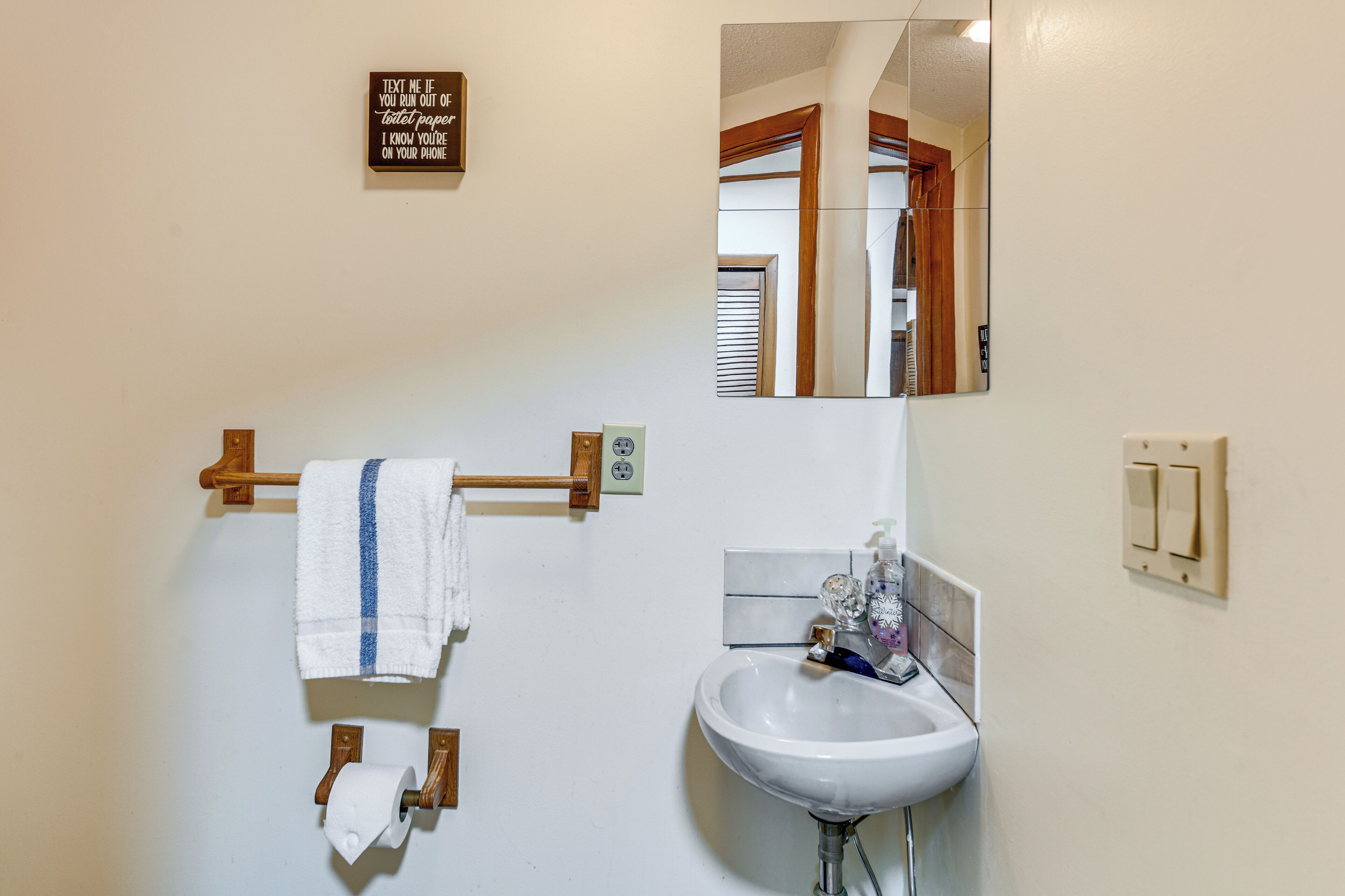 A bathroom with a white sink, a towel rack with a white towel, a toilet paper holder, a mirror, and a sign above the sink.