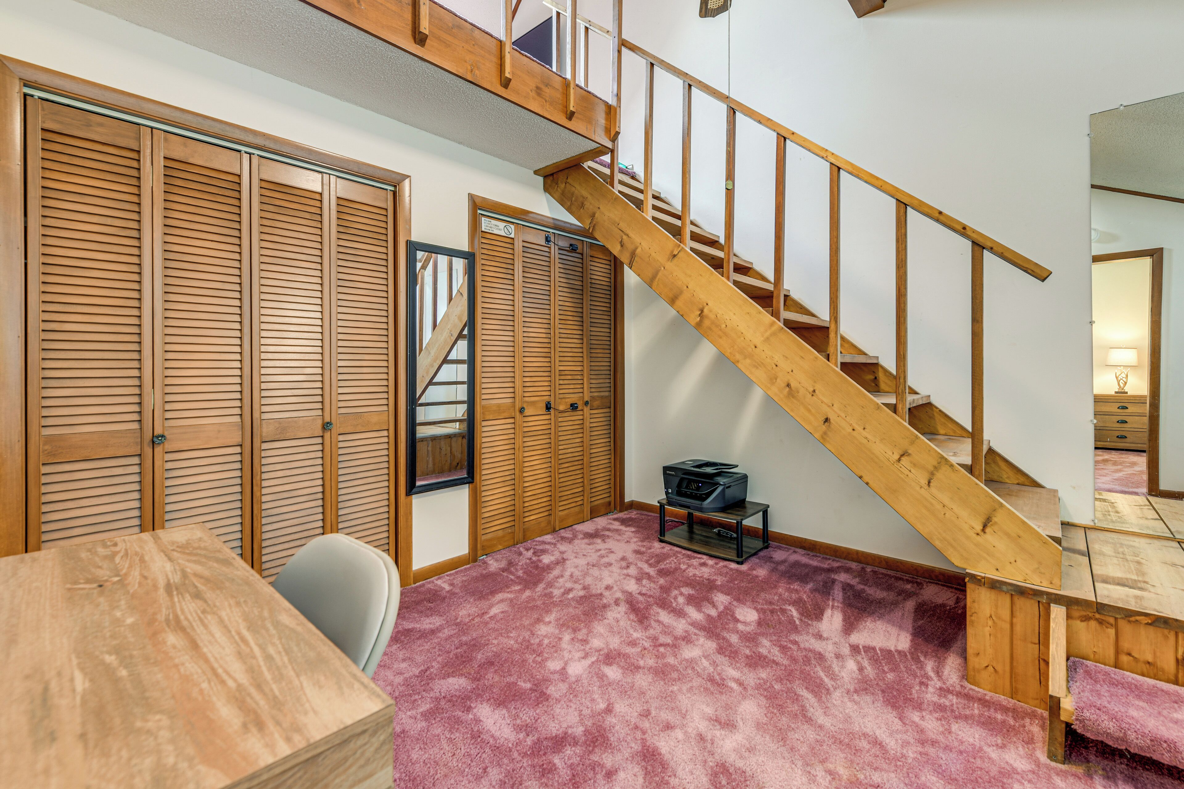 A room with a wooden staircase, a closet with sliding doors, a small table, and a chair.
