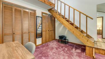 A room with a wooden staircase, a closet with sliding doors, a small table, and a chair.