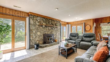 A spacious living room with a stone fireplace, leather sofa, and large windows offering a view of the outdoors.