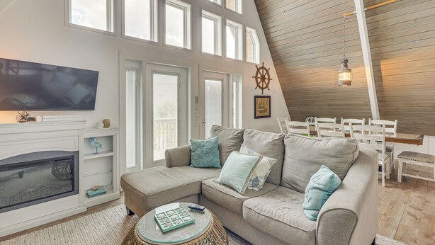 A cozy living room with a fireplace, a large window, and a high ceiling.