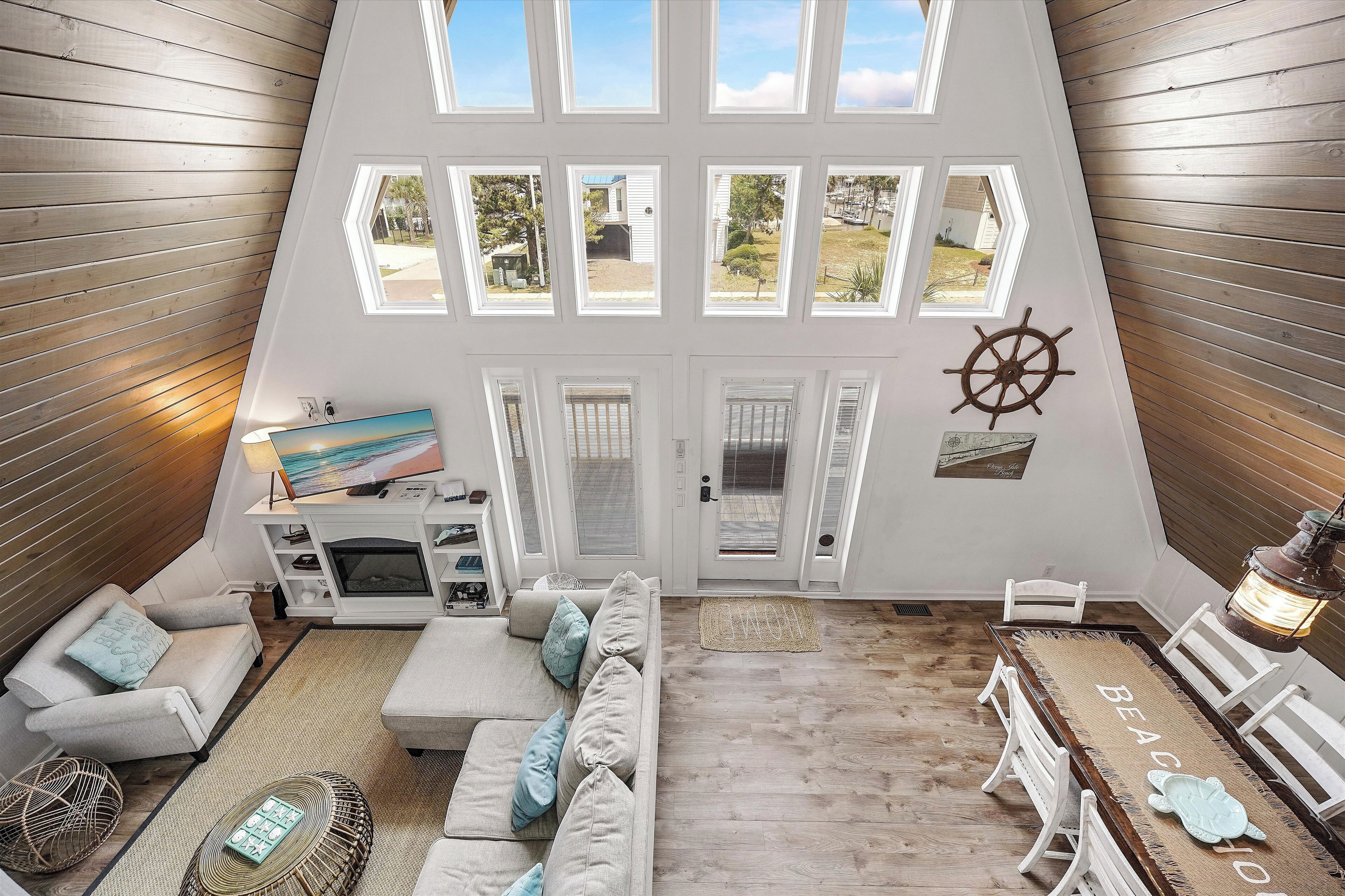 Ein geräumiger Wohnbereich mit hoher Decke, Holzwänden und einem großen Fenster mit Blick auf einen Garten.