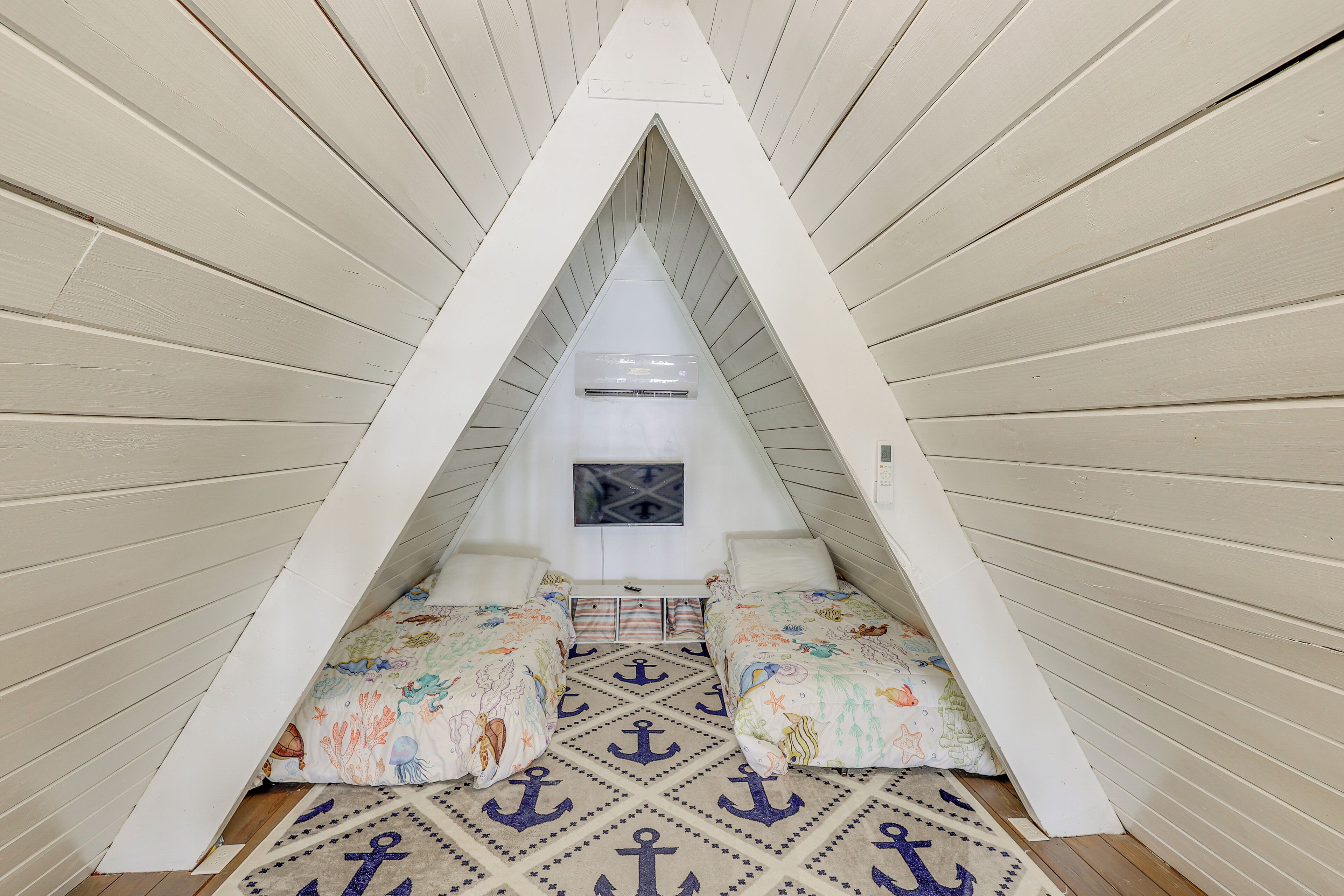 A triangular attic room with a sloped ceiling, a small window, and a bed with colorful bedding.
