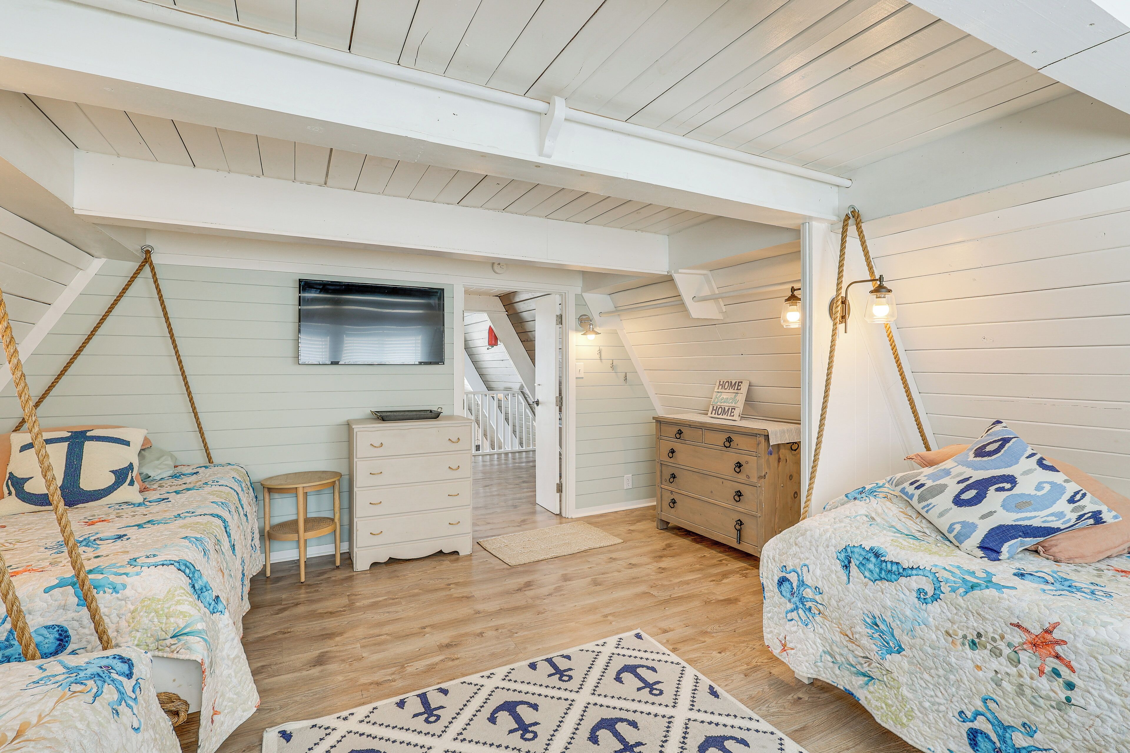 A bedroom with a loft-style ceiling, wooden flooring, and nautical-themed bedding.