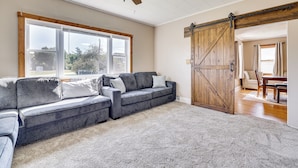 A living room with a sectional sofa, a ceiling fan, a large window, and a barn-style door. - Merrillan Getaway w/ Kayaks & ATV Trail Access! (Merrillan)