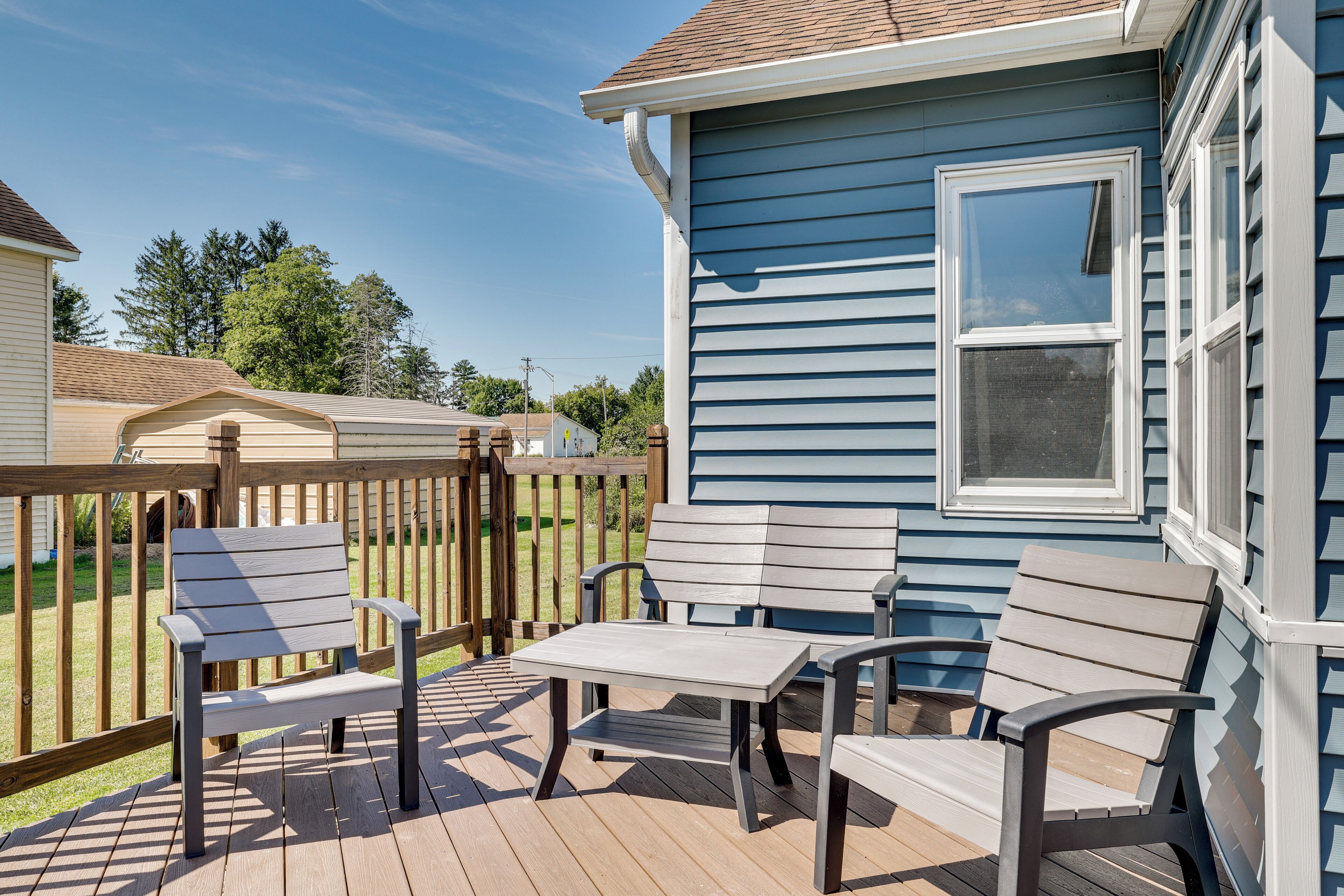A deck with a table and two chairs, a wooden fence, and a house with blue siding and a white window.