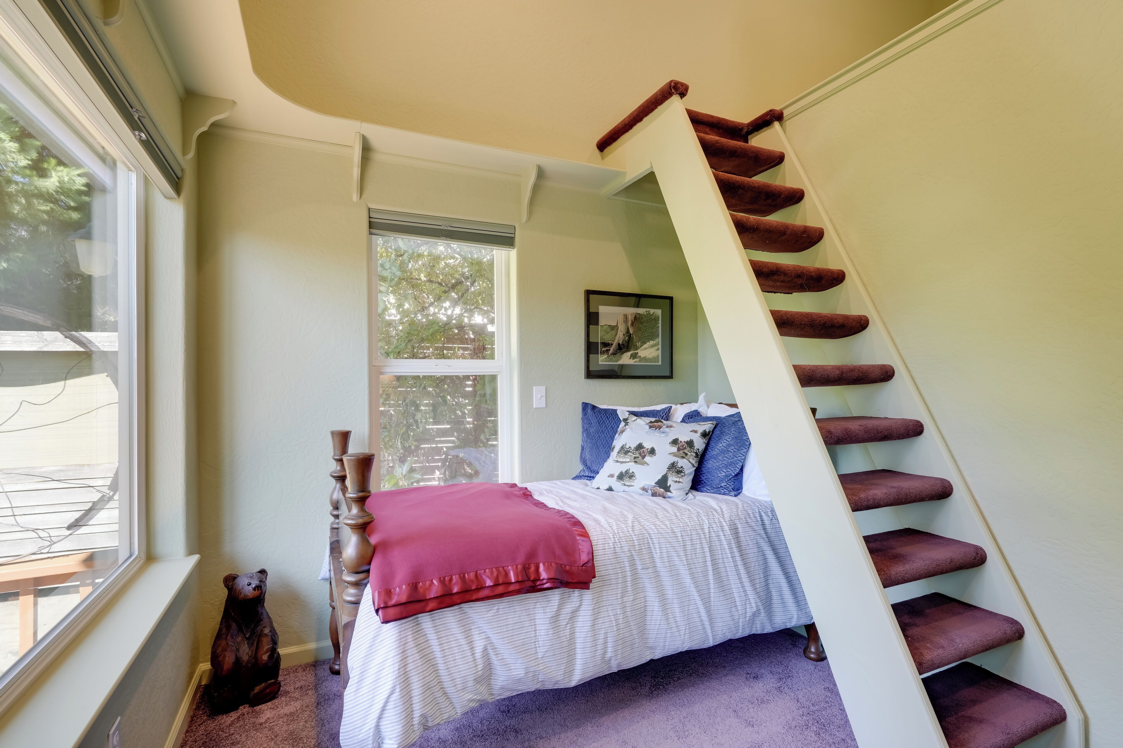 A bedroom with a bed, a window, a staircase, and a teddy bear.