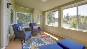 A sunroom with wicker furniture, a patterned rug, and large windows offering a view of trees and a body of water. - On Mckenzie River! Home w/ Scenic Sunroom (Vida)